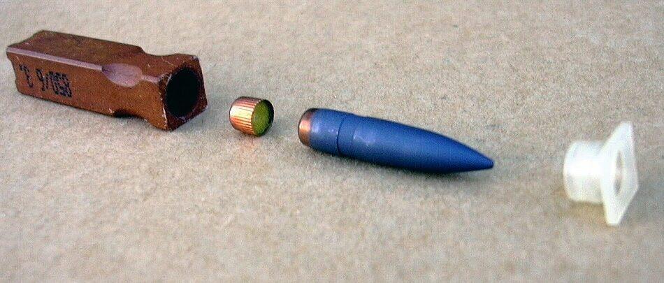 The 4.73×33 mm caseless ammunition used in the Heckler & Koch G11 rifle, shown disassembled. The components are, from left to right, the solid propellant, the booster, the bullet, and a plastic cap that serves to keep the bullet centered in the propellant block.