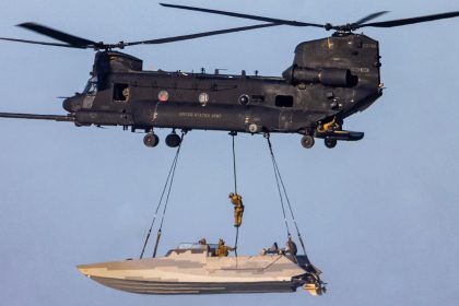 one of an MH-47 Chinook sling loading a stealthy Combat Craft Assault (CCA) boat while one of its crew, most likely a SWCC, fast ropes down into it in mid-air.