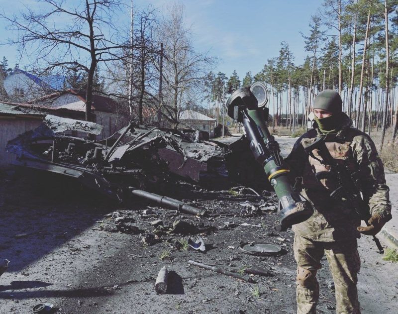 Ukrainian soldier posing in front of destroyed tank with NLAW