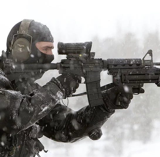 Special operations forces operator aiming through reflex sight on Colt Canada C7 rifle