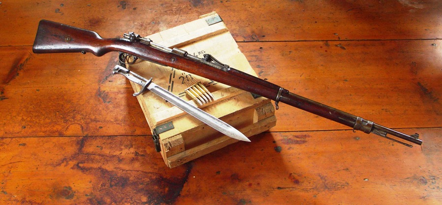 A Mauser Gewehr 98 (M98) rifle on a wooden box with ammunition and a dagger lying nearby