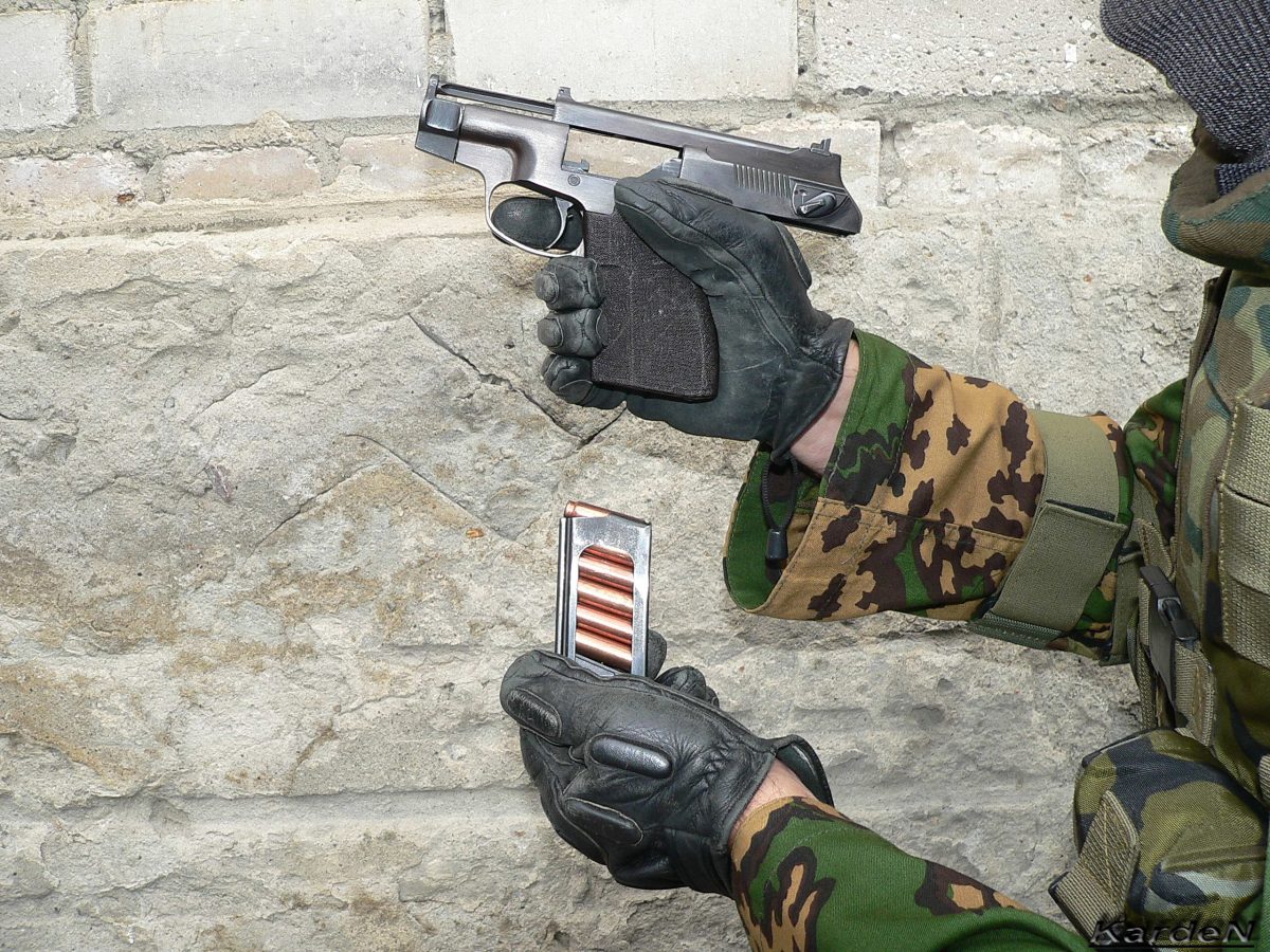 A soldier holding a black PSS silent pistol with the magazine removed
