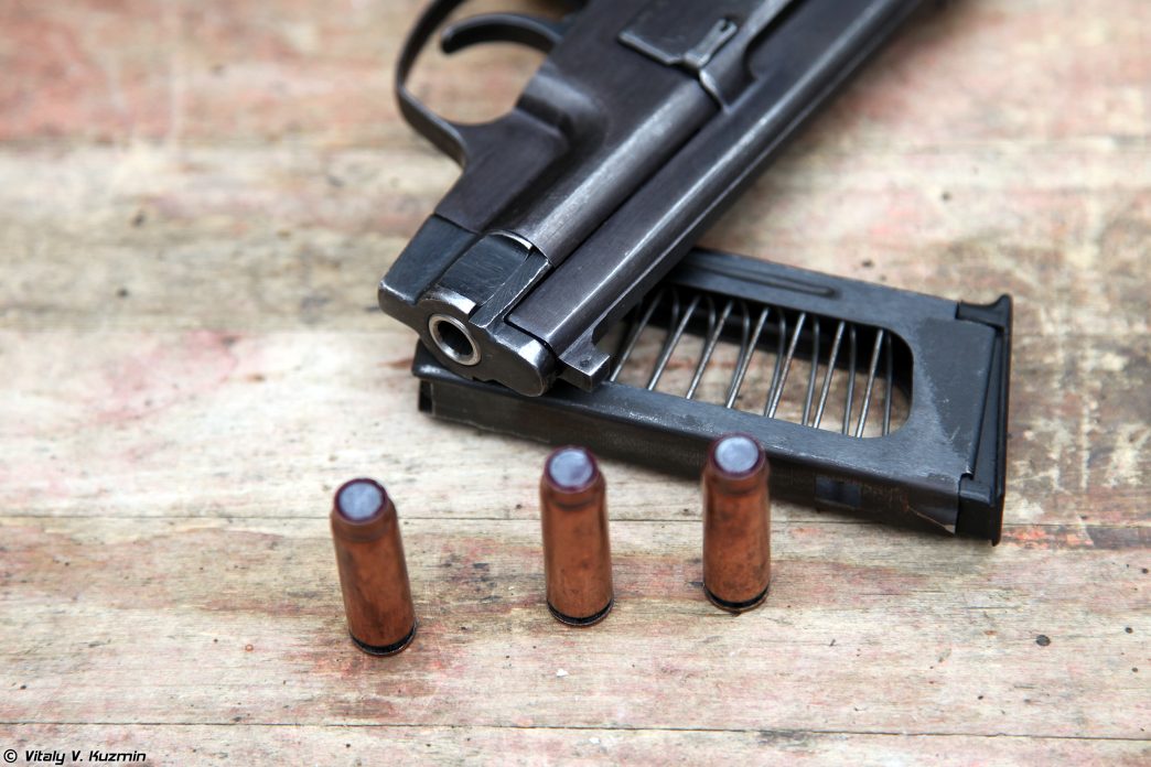 A black PSS silent pistol lying on a surface with an empty magazine and several rounds of ammunition scattered beside it