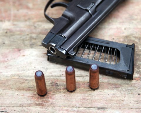 A black PSS silent pistol lying on a surface with an empty magazine and several rounds of ammunition scattered beside it