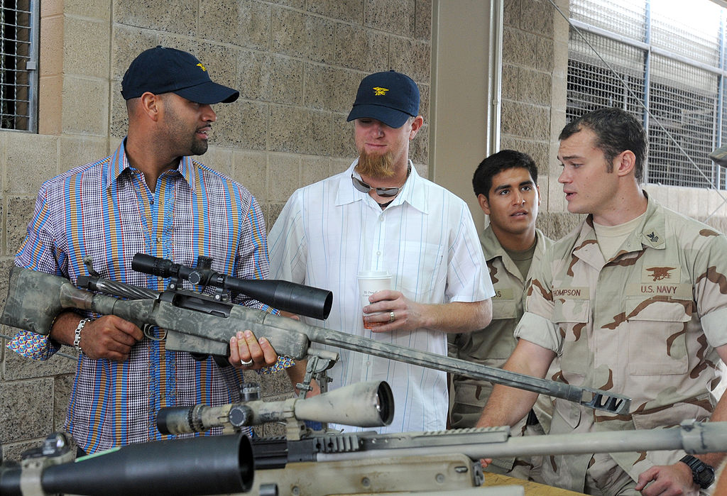 Special Warfare Operator 1st Class Thompson explains details of an Mk 15 sniper rifle to major league baseball players Albert Pujols and Ryan Franklin during a tour of Naval Special Warfare facilities