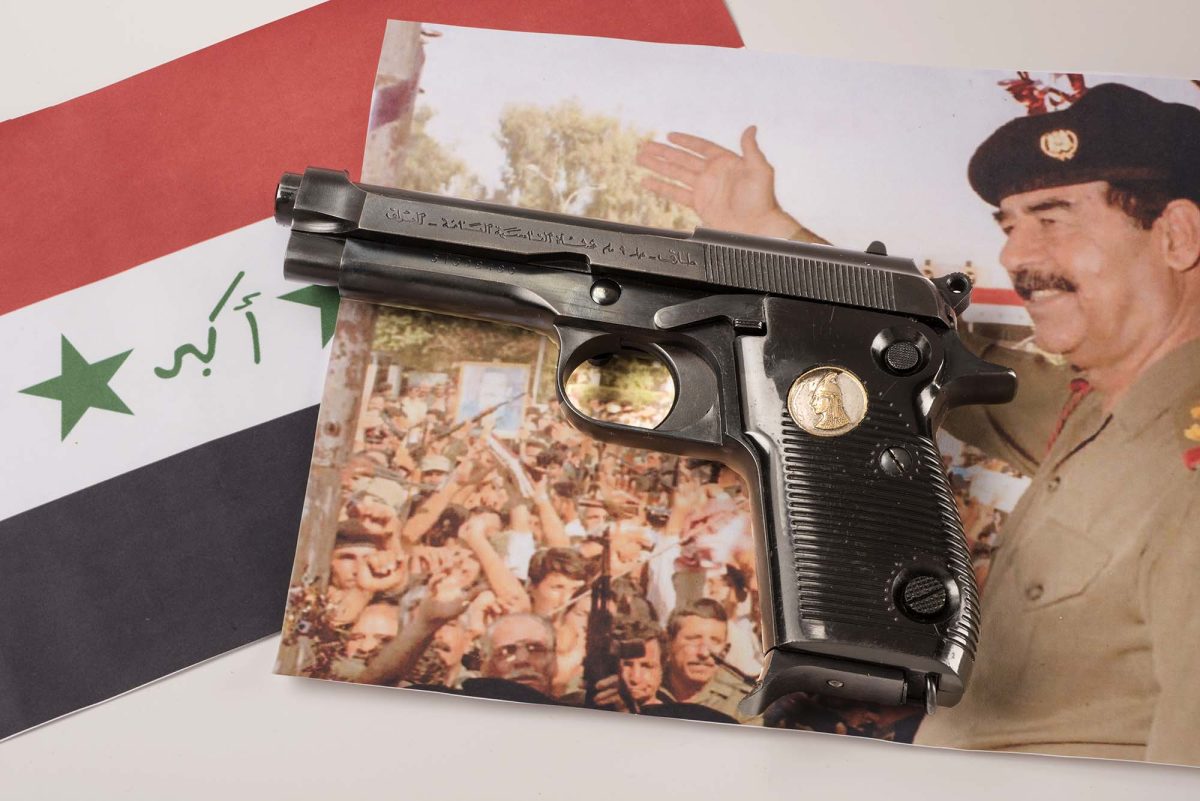 A Tariq 9mm pistol on a table with a picture of Saddam Hussein in the background
