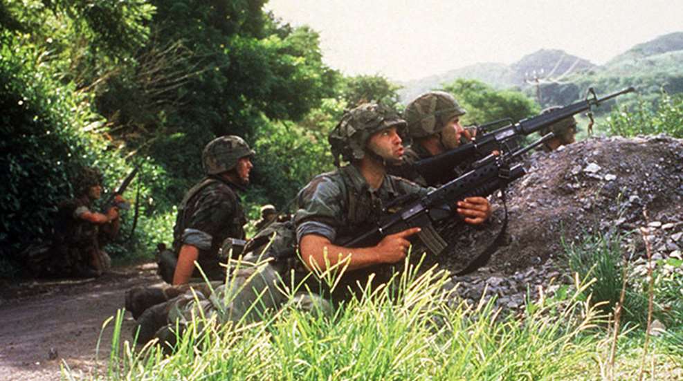 A group of soldiers armed with rifles lying in cover during Operation Urgent Fury